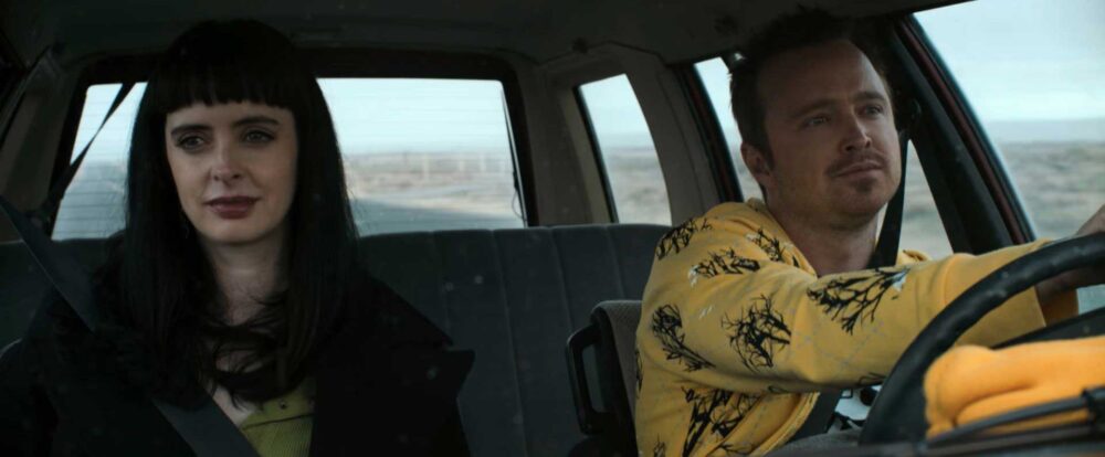 A still from the movie El Camino featuring Aaron Paul and Krysten Ritter driving in a car.